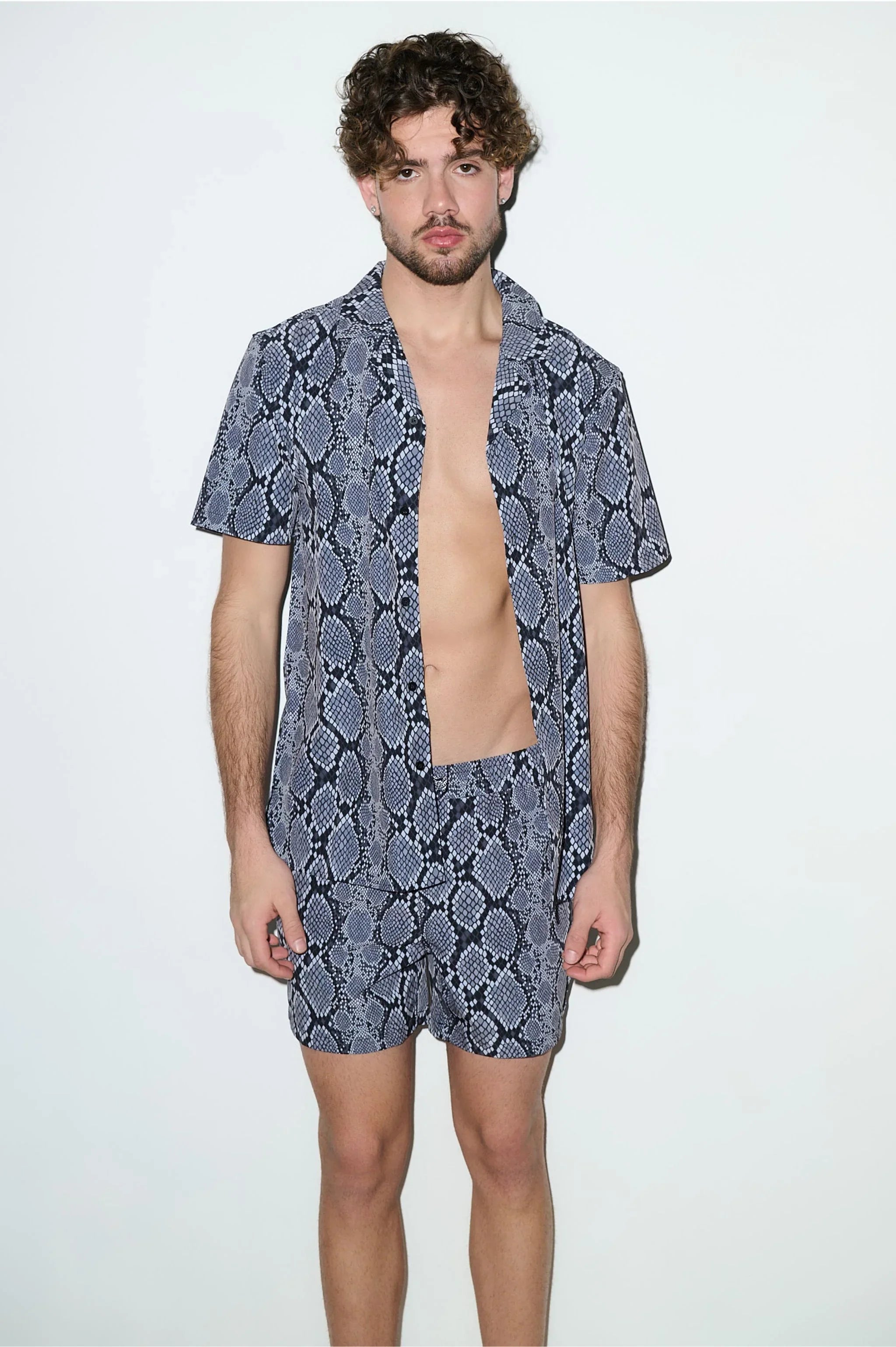 Man wearing matching snake print cabana shirt and shorts set, standing against white background.