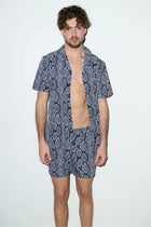 Man wearing matching snake print cabana shirt and shorts set, standing against white background.