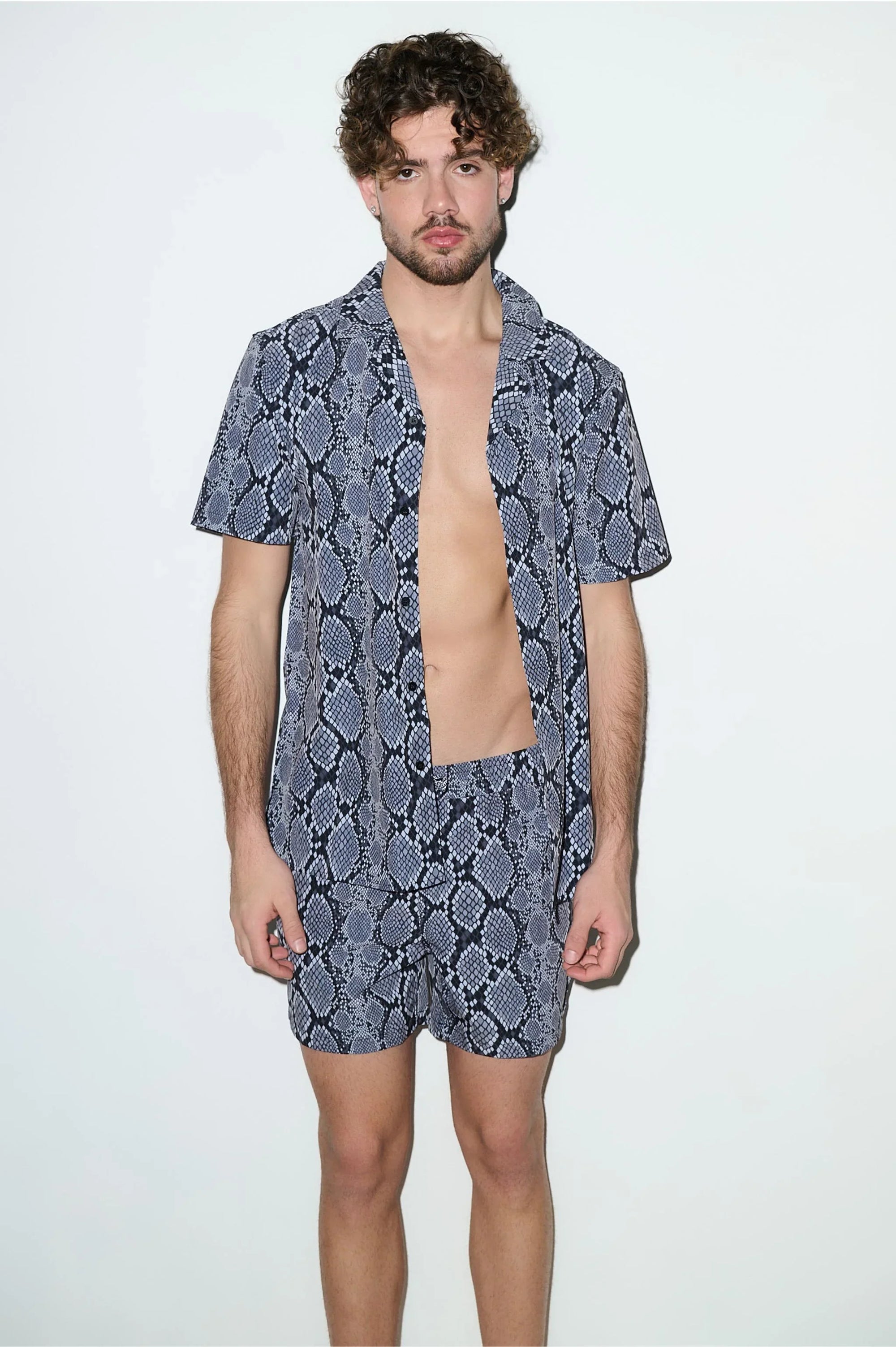 Man wearing matching snake print cabana shirt and shorts set, standing against white background.