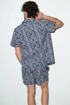 Man wearing short-sleeve cabana set with black and grey snake print, shown from the back