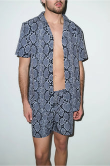 Man wearing short-sleeve shirt and shorts cabana set with blue snake print pattern
