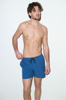 Male model wearing petrol blue men's swim trunks with drawstring waist