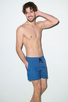 Man modeling petrol blue men's swim trunks with drawstring waistband against white background