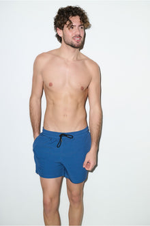 Man modeling petrol blue volley swim trunks with drawstring waist against white background