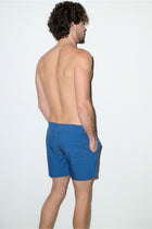 Man modeling petrol blue men's swim trunks with back pockets, side view, studio setting